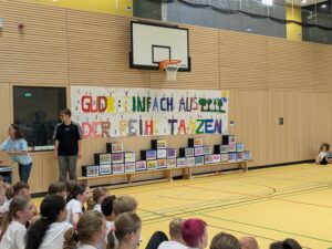 Turnhalle mit Transparent "GUDB einfach aus der Reihe Tanzen", einer leeren Tanzfläche und einigen Schulkindern