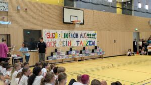 Turnhalle mit Transparent "GUDB einfach aus der Reihe Tanzen", einer leeren Tanzfläche und einigen Schulkindern